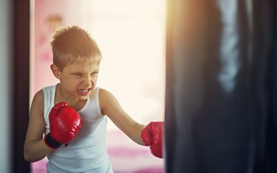 Little boy wearing boxing gloves hitting punching bag