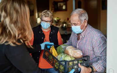 Woman delivering groceries to an older couple wearing face masks