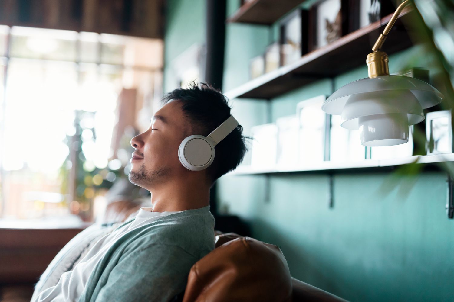 homme les yeux fermés, profitant de la musique avec des écouteurs, se relaxant sur le canapé à la maison